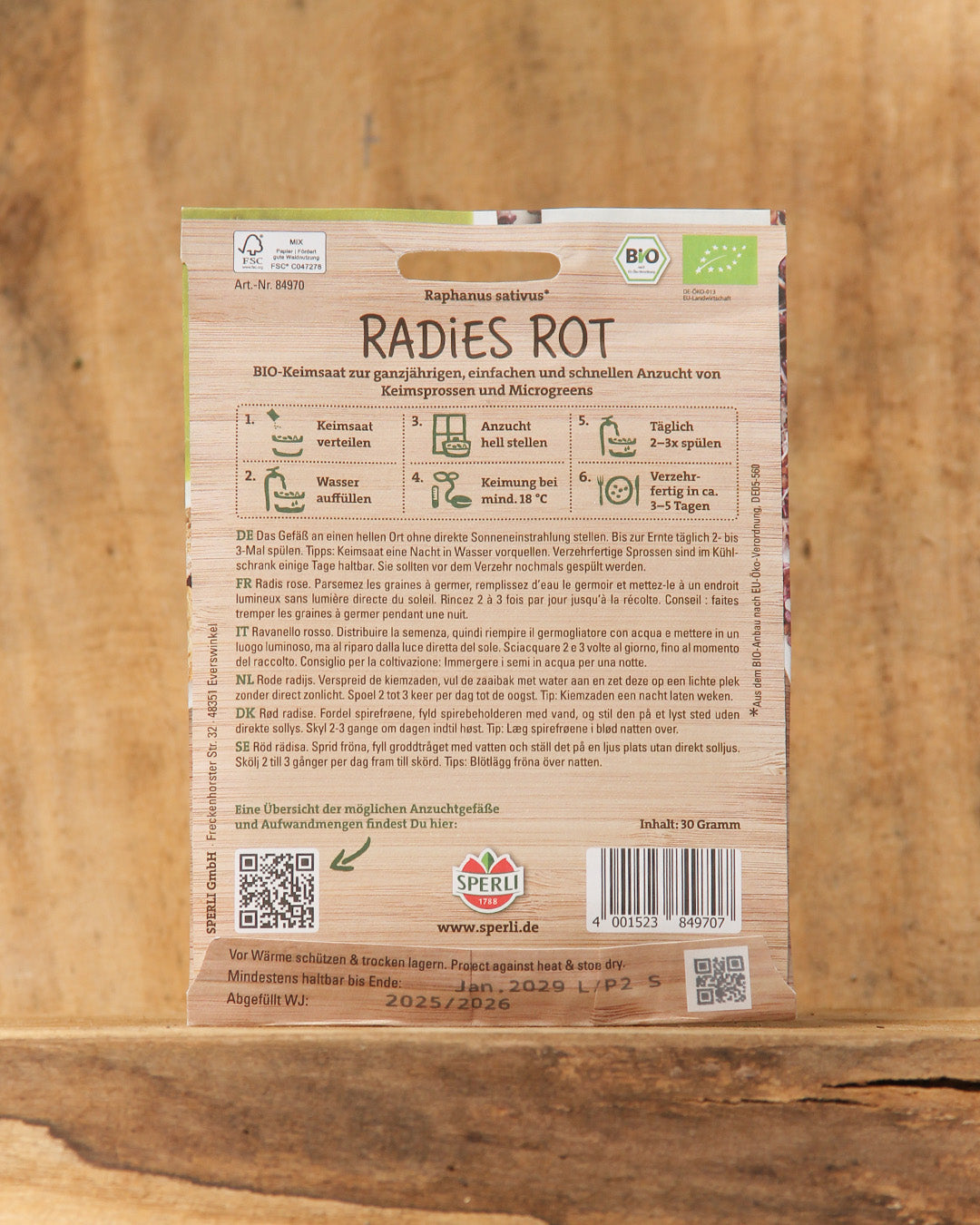 Eine Packung Sperli's Bio Keimsprossen Saatgut 'Radies Rot', mit deutscher Anleitung, QR-Codes, Bio-Logos und einem Holzhintergrund.