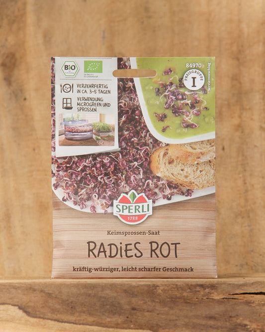 Eine Packung Bio Keimsprossen Saatgut 'Radies Rot' von Sperli ist auf einer Holzfläche ausgestellt, auf der Abbildungen von roten Sprossen auf Brot und in einer Schale sowie Bio- und Zertifizierungssymbole zu sehen sind.