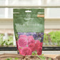 Ein grüner und rosafarbener 600-g-Beutel David Austin | Langzeitdünger für Rosen liegt auf einem Tisch in einem Gewächshaus, umgeben von Topfpflanzen und Setzlingen - perfekt für gesundes Rosenwachstum und starke Wurzeln.