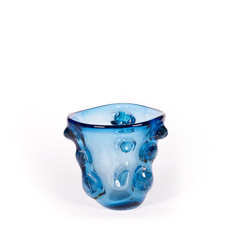Die Des Pots | Skulpturale Vase blau aus Glas (H 22 Ø 20 cm) zeichnet sich durch eine unregelmäßige Form mit abgerundeten Erhebungen und dezenten Blau-Weiß-Design-Akzenten aus, die vor einem schlichten weißen Hintergrund gezeigt wird.