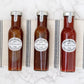Drei Glasflaschen mit Soßen – „Wilkin & Sons Tiptree Steak Sauce Rauchig würzig“, „typisch englische Würzsauce (Brown Sauce)“ und Tomatenketchup – stehen in einer Reihe auf einem gestreiften Tuch, das auf einer weißen Marmorplatte liegt.