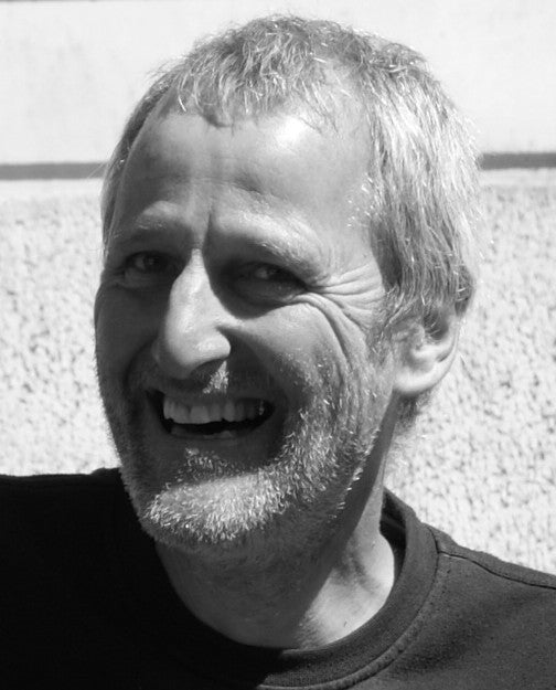 Ein Mann mittleren Alters mit kurzen, graumelierten Haaren und Bart lächelt breit. Er trägt ein dunkles Hemd, und im Hintergrund des schwarz-weißen Fotos ist eine strukturierte Wand zu sehen – vielleicht wurde das Bild aufgenommen, nachdem er den Kurs der Königlichen Gartenakademie absolviert hatte. 16.1.2027 | TAGESKURS 9.30 – 16.30 Uhr „Schnitt von Obstbäumen und Sträuchern für Hobbygärtner“.