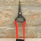 Die Blumenschere Niwaki | 'Forged Snips' mit roten Griffen und spitzen Klingen steht aufrecht an einer strukturierten Steinwand. Ein schwarzes Band in der Nähe der Griffe zeigt die präzise Handwerkskunst dieser japanischen Gartenschere von Niwaki.