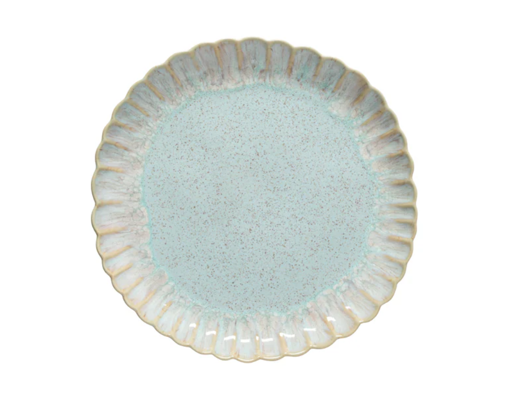 Der Costa Nova Speiseteller "Mallorca meerblau" (Ø 27 cm, H 3,3 cm) ist ein runder Keramikteller mit einem gewellten, strukturierten Rand und einem hellblau gesprenkelten Zentrum, inspiriert von portugiesischer Handwerkskunst. Der Teller steht auf weißem Hintergrund.