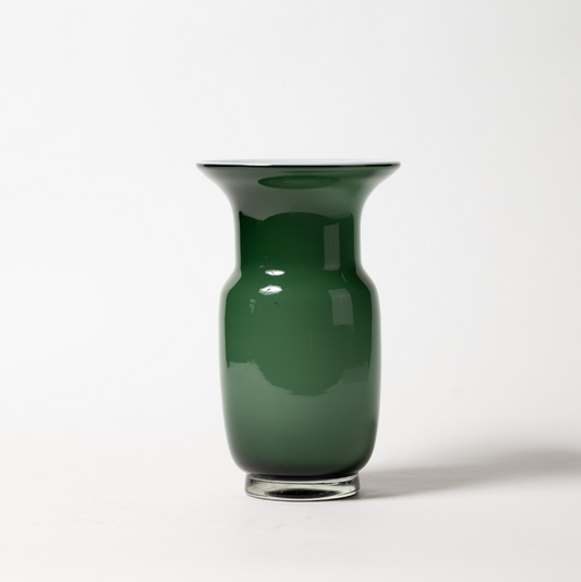 Die Des Pots Grün Vase aus Glas in Kelchform (H 27 cm, Ø 17 cm) mit glänzender, reflektierender Oberfläche und leicht zulaufendem Sockel steht auf weißer Fläche vor schlichtem Hintergrund.