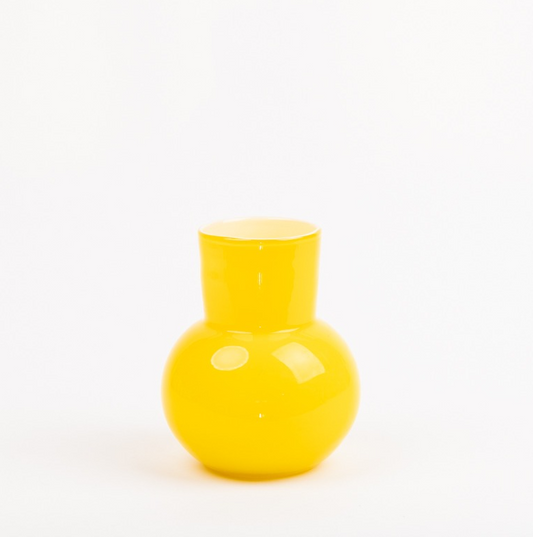 Die Des Pots | Gelbe Vase aus Glas (H 21 Ø 18 cm) von Des Pots präsentiert sich glänzend und rund mit schmalem Hals und breitem Fuß als stilvolles Wohnaccessoire vor schlichtem, weißem Hintergrund.