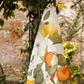 Das Napking | Premium Leinen Geschirrtuch 'Amalfi' (55 × 75 cm) zeigt ein lebhaftes Zitrusfrucht- und Blumendesign und bringt mediterranen Charme in Ihre Küche. Das Geschirrtuch hängt im Freien an einer rustikalen Steinwand. Marke: Napking.