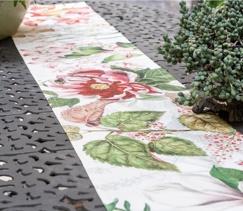 Die Nahaufnahme eines Tisches im Freien zeigt den Napking Premium Leinen Tischläufer 'Dafne' 50 x 150 cm und eine eingetopfte Sukkulente auf der rechten Seite, die das elegante florale Muster des Läufers von Napking hervorhebt.