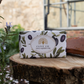 Eine ESC | 'Olive' Luxuriöse Olivenölseife mit mediterranem Duft von The English Soap Company liegt in olivenverziertem Papier verpackt auf einem Baumstumpf im Freien neben einer Pflanze und einem Ziegelstein.