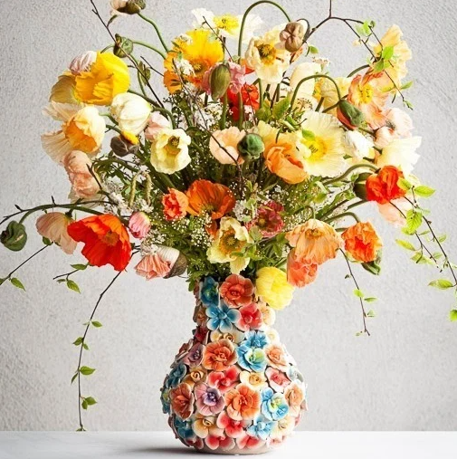 „The Des Pots | Vase mit bunten Deko-Blumen (H 17, Ø 5,5–14 cm)“ von Des Pots ist eine farbenfrohe Keramikvase, die mit bunten, plastisch gestalteten Blumen verziert ist – ideal als fröhlicher Akzent auf jedem schlichten, hellen Hintergrund.