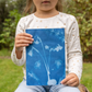 Ein kleines Kind sitzt draußen im Garten, trägt ein cremefarbenes Hemd mit goldenen Sternen und hält einen blau-weißen botanischen Druck in der Hand, der auf Esschert Solar Fotopapier A5 (12 Blatt für kreative Sonnenbilder) erstellt wurde.