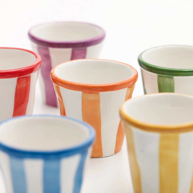 Sechs Keramikbecher mit bunten vertikalen Streifen in Rot, Orange, Gelb, Grün, Blau und Violett sind auf einer weißen Fläche angeordnet. Inspiriert von der farbenfrohen Kollektion „Zafferano Lido Righe Tasse Gelb 7 cl“ von Zafferano besticht jeder Becher durch kräftige Streifen und einen farblich abgestimmten Rand, was ihm eine fröhliche und moderne Note verleiht.