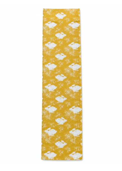 Verleihen Sie Ihrer Tischdekoration eine verspielte Note mit dem Tischläufer „Sam Wilson | Headlong Hare“ in der Farbe „Yellow Ochre“ (34 × 196 cm) – einem langen, gelben, rechteckigen Tuch mit einem sich wiederholenden Muster aus weißen Hasen und Blumen der Marke Sam Wilson.