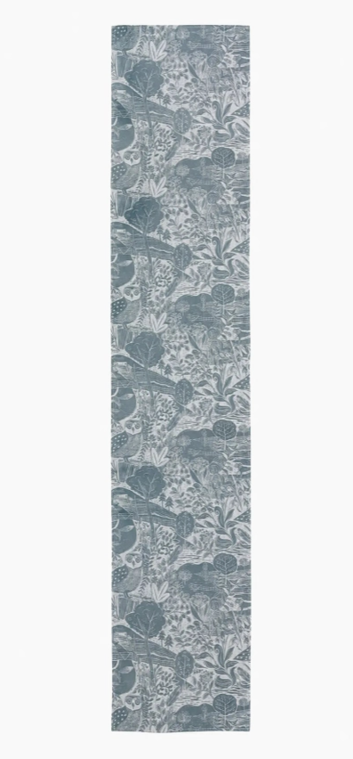 Ein langer, schmaler Tischläufer von Sam Wilson mit dem Motiv „Owl & Fox“ im Format 34 × 196 cm, der in einem gedeckten Graublau gehalten ist und ein filigranes botanisches Muster aus verschiedenen Blättern und Pflanzen aufweist.