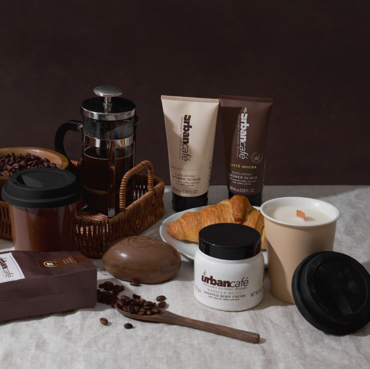 Die Handseife „Urban Caffé Mocha“ (500 ml) von Somerset Toiletry, angereichert mit Kaffeeextrakt, wird kunstvoll neben einer French Press, Kaffeebohnen, Croissants, einer brennenden Kerze und einem Kaffee-To-Go-Becher auf einem Tisch vor einem neutralen Hintergrund präsentiert.