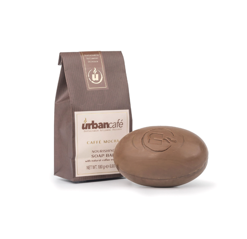 Neben einer runden braunen Seife mit einem eingeprägten U-Logo steht eine braune Tüte mit der Aufschrift „Somerset Toiletry Handseife | Urban Caffé Mocha Seifenstück 180 g“; beide sind auf weißem Hintergrund abgebildet. Diese mit Kaffeeextrakt und Kakaobutter angereicherte Seife sorgt für ein reichhaltiges, verwöhnendes Reinigungserlebnis.