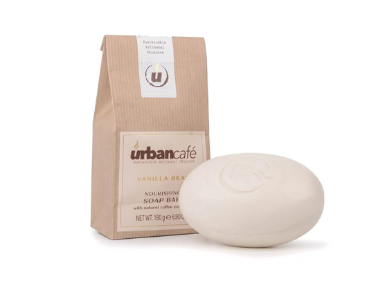 Eine beigefarbene Handseife | „Urban Caffé Vanilla Soap Bar“ 180 g von Somerset Toiletry liegt vor einer braunen Papierverpackung, die mit dem „urbancafé“-Branding, dem runden Logo und der Aufschrift „Vanilla Bean Nourishing Soap Bar“ versehen ist. Diese Seife enthält Sheabutter und Kaffeeextrakt und sorgt für eine sanfte, pflegende Reinigung.