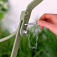 Eine Hand setzt einen Metallstift an einer Kette in den Rahmen des Harrod | Bistro Set 'Darsham' Klappbarer Gartentisch mit 2 Stühlen in Salbeigrün von Harrod Horticultural ein, wobei das Grün im Hintergrund sanft verschwimmt.