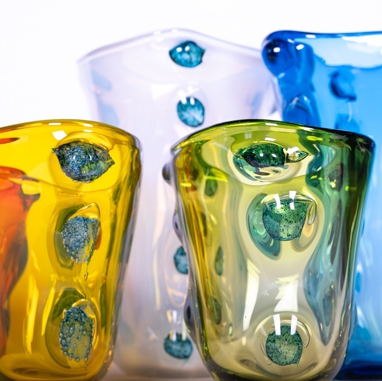 Die Des Pots | Skulpturale Vase grün aus Glas (H 22 Ø 20 cm) von Des Pots ist eine grüne Glasvase mit skulpturalem Design und wellenförmiger Textur, die sich vor einem weißen Hintergrund präsentiert.