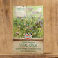 Eine 450-g-Packung der Sperli's Gründüngermischung Bodenkur 'Vital-Grün' steht aufrecht auf einer Holzfläche und zeigt den Markennamen und die Produktangaben in deutscher Sprache mit abgebildeten blühenden Pflanzen vor einem verschwommenen Holzhintergrund.