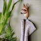 Der Wildlife Garden Handgeschnitzter Wandhaken aus Lindenholz 'Alpaka' von Wildlife Garden hält einen beige-weißen Strickpullover. Neben dem originellen Haken sind grüne Pflanzen und Blätter an der hellen Wand zu sehen.