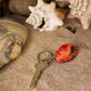 A Wildlife Garden Handgefertigter Schlüsselanhänger aus Holz in Oktopus-Form liegt auf Sand umgeben von Muscheln und einer großen Muschel - ein ideales maritimes Geschenk.