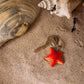 Ein Wildlife Garden | Handgefertigter Schlüsselanhänger aus Holz | Seestern liegt am Sandstrand neben großen Muscheln und präsentiert sein maritimes Design.