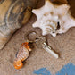 Der Wildlife Garden Handgefertigter Schlüsselanhänger aus Holz Seepferd liegt mit einem silbernen Schlüssel auf Sand neben einer großen Muschel - das perfekte maritime Accessoire für Strandliebhaber von Wildlife Garden.