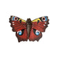 Handgeschnitzter "Schmetterling Tagpfauenauge" Magnet von Wildlife Garden, mit einem Schmetterling mit dunkelroten Flügeln und blauen, gelben und schwarzen Augenmustern. Von oben auf weißem Grund betrachtet - ideal, um jeden Raum zu erhellen.