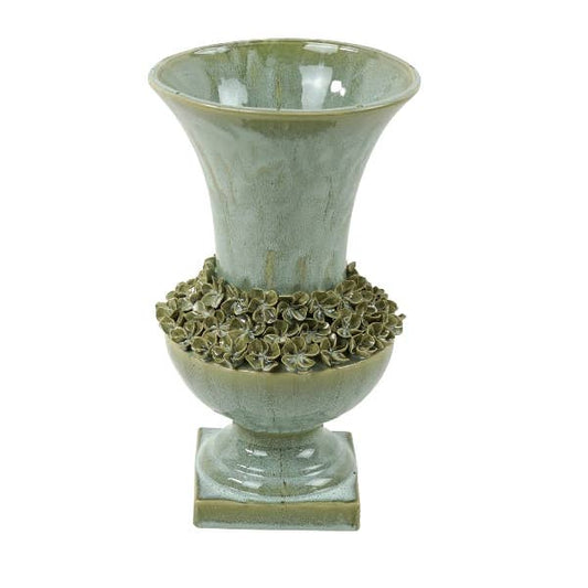 Wir präsentieren die „Amphore“ von Werner Voß: eine mediterran inspirierte Vase aus grünem Steingut (25 x 41,5 cm) mit dekorativen floralen Details, die den mittleren Bereich umgeben, einem breit auslaufenden Rand und einem eleganten quadratischen Sockel.