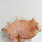 Die rosa Dekoschale „Fazzoletto“ aus Murano-Glas (H 20, Ø 22 cm) von Murano Dream glänzt mit ihrem gewellten Rand auf weißem Marmor und verkörpert die Eleganz der italienischen Glaskunst.