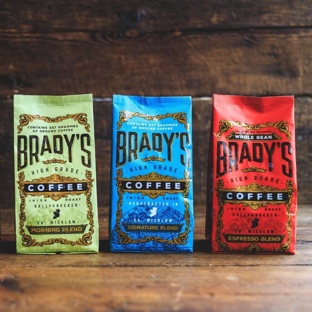 Drei farbenfrohe Tüten der Brady's Coffee Company mit dem 227 g gemahlener Signature Blend Kaffee sind nebeneinander auf einer Holzfläche mit rustikalem Holzhintergrund angeordnet.