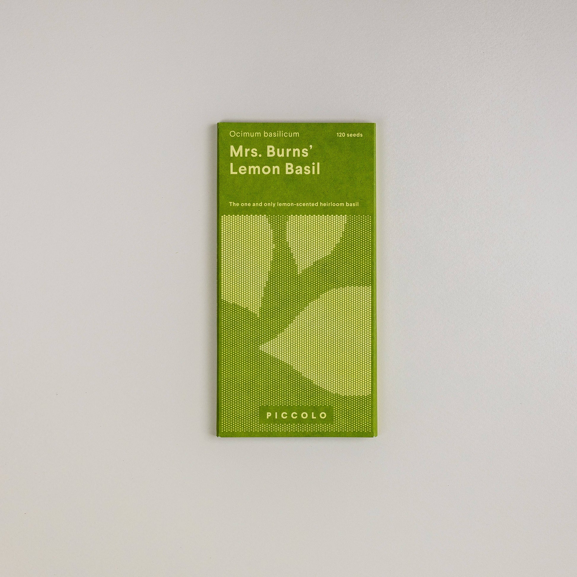 Ein grünes Päckchen Piccolo Seeds | Basilikum Mrs. Burns Zitrone ist auf einem weißen Hintergrund zentriert, mit Blattillustrationen und Text, der dieses nach Zitrone duftende, aromatische Erbstück von Piccolo Seeds beschreibt.
