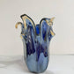 Die Murano Dream – eine mittelgroße „Giusy“-Vase aus blauem Murano-Glas (H 24, Ø 19 cm) mit gewellten Rändern – steht auf weißem Marmor und präsentiert feine italienische Glaskunst vor einem schlichten, hellen Hintergrund.