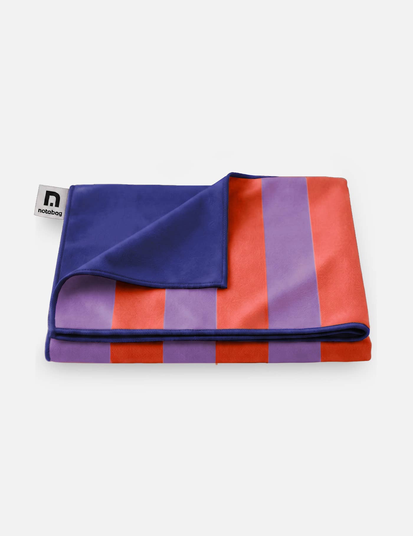 Das „Notabag | Handtuch rot & lila gestreift 78 × 160 cm“ von Notabag ist ein gefaltetes Handtuch mit breiten roten und violetten Streifen, dunkelblauer Rückseite, aus recyceltem Material, schnell trocknend und mit einem Logo-Etikett, abgebildet auf einem schlichten weißen Hintergrund.