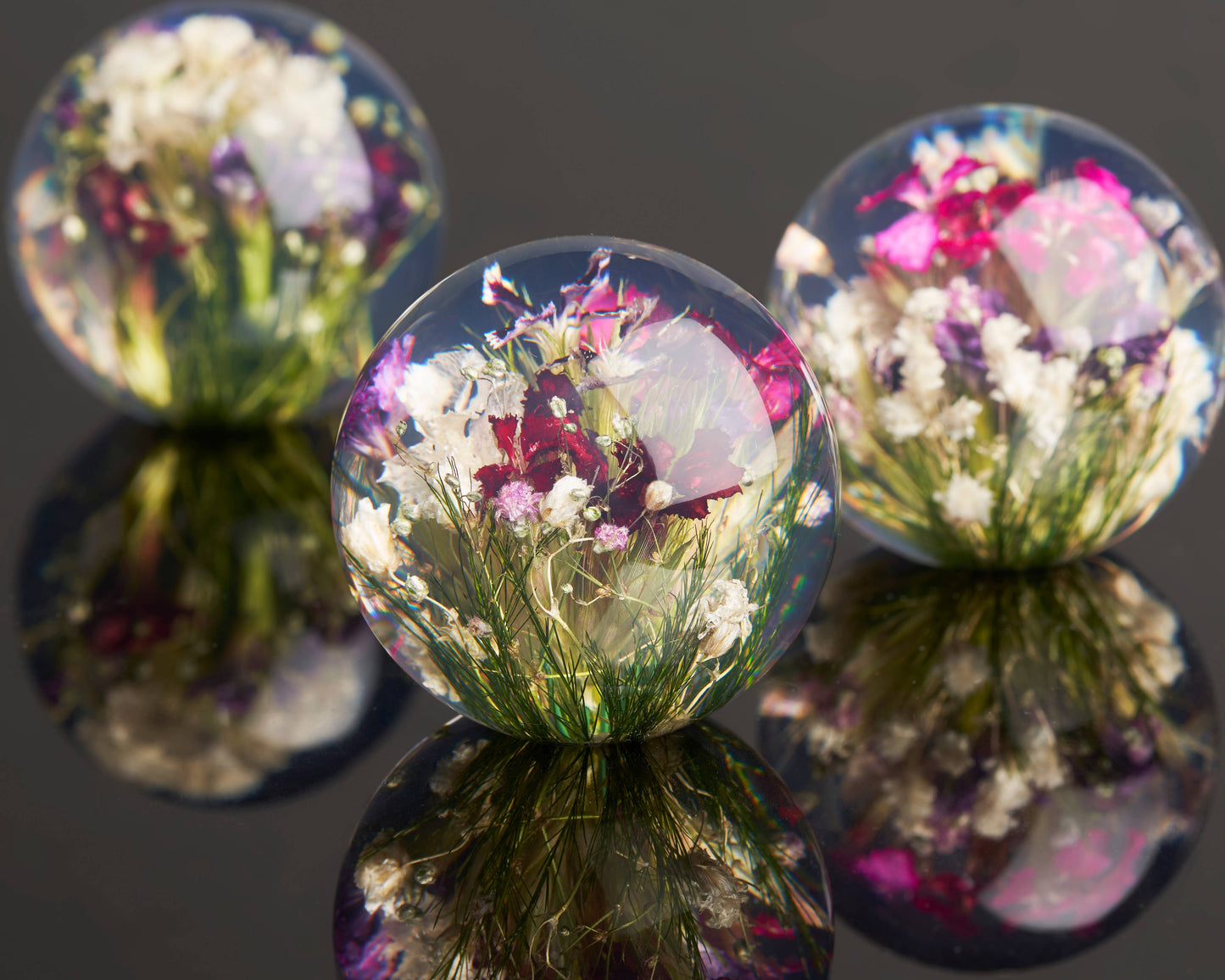 Der Hafod Grange | Briefbeschwerer mit gemischter Flora besteht aus drei klaren Harzkugeln mit farbenfrohen getrockneten Blumen, darunter Mini-Dianthus - ein kunstvolles Schreibtisch-Accessoire von Hafod Grange, das jeden Arbeitsbereich aufwertet.