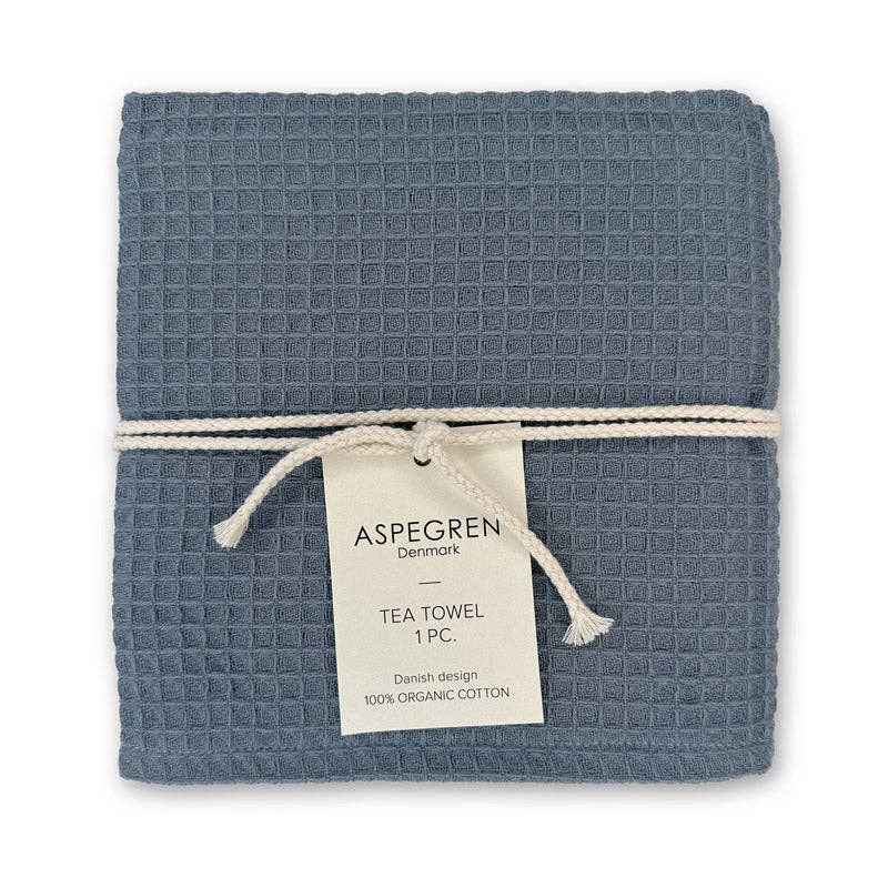 Ein gefaltetes blaues Geschirrtuch mit Waffelmuster, gefertigt aus 100 % Bio-Baumwolle und mit einer weißen Schnur zusammengebunden. Auf dem Etikett steht: „Aspegren Denmark | Premium-3er-Geschirrtuchset in tiefen nordischen Blautönen. Dänisches Design, 100 % Bio-Baumwolle.“ Eine stilvolle Ergänzung für Ihre Küchentextilien oder das perfekte Geschenkset von Aspegren Denmark.