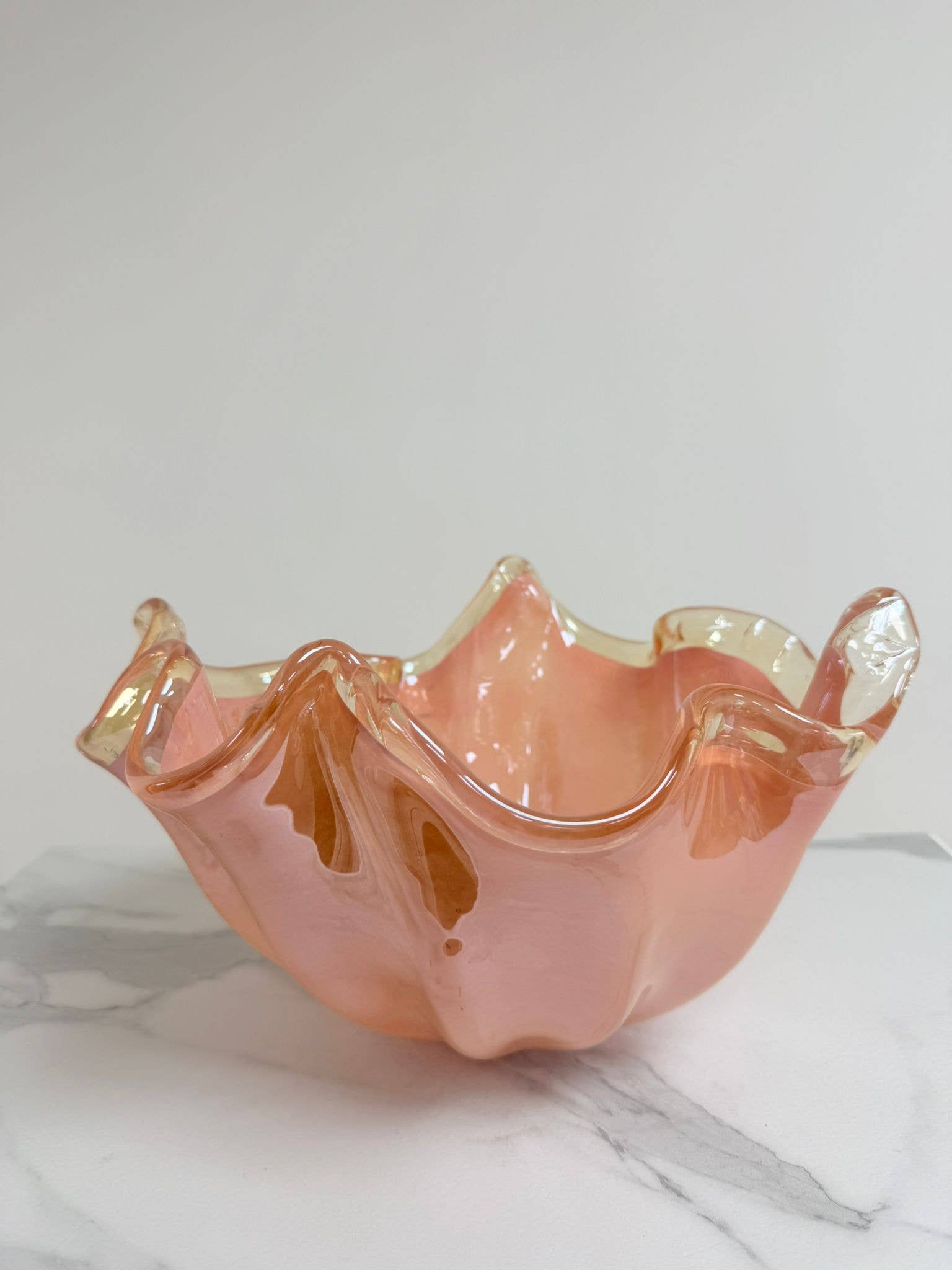 Die Murano Dream Dekoschale „Fazzoletto“ aus rosa Murano-Glas (H 20, Ø 22 cm) mit glänzender Oberfläche steht auf weißem Marmor vor einem hellen Hintergrund.