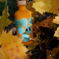 Eine 200-ml-Flasche Yiayia and friends | Weißer Balsamico-Essig mit blauen Kreisen und Cartoon-Augen auf dem Etikett ruht inmitten gelber Herbstblätter - ideal für eine natürliche Vinaigrette ohne Zusatzstoffe.