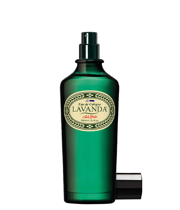 Ein grüner Glasflakon von Ach.Brito Eau de Cologne | Lavander 100 ml mit Sprühkopf und schwarzer Kappe in der Nähe, mit einem cremefarbenen Etikett mit dekorativen Rändern.