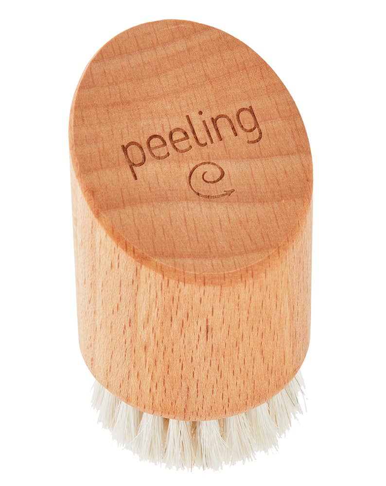 Die Croll & Denecke Gesichtsbürste aus Holz für Peeling & Massage ist eine kleine, ovale Gesichtsbürste aus Buchenholz mit weichen, weißen Borsten, dem eingravierten Wort "Peeling" und einem Spiralsymbol.