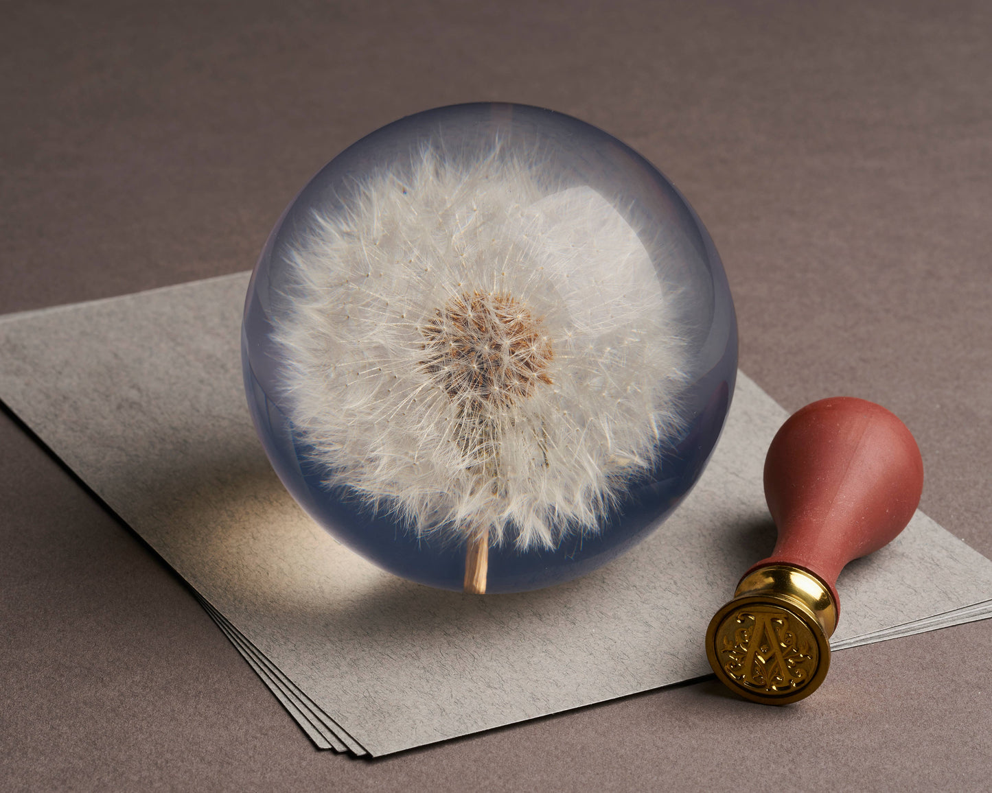 A Hafod Grange | Briefbeschwerer mit Löwenzahn von Hafod Grange liegt auf grauem Papier neben einem roten Wachssiegelstempel-ein elegantes Schreibtisch-Accessoire für jeden Arbeitsplatz.