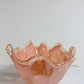 Die Murano Dream Dekoschale „Fazzoletto“ aus rosa Murano-Glas (H 20 cm, Ø 22 cm) mit gewellten Rändern und goldenem Rand glänzt auf einer weißen Marmorfläche vor einem schlichten, hellen Hintergrund.