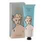 Eine blau-weiße Tube Archivist | 'Kokosnuss' Handcreme von Archivist Gallery mit der Aufschrift "göttliche Handcreme" und einem illustrierten Frauengesicht steht neben der passenden Schachtel mit demselben Design.