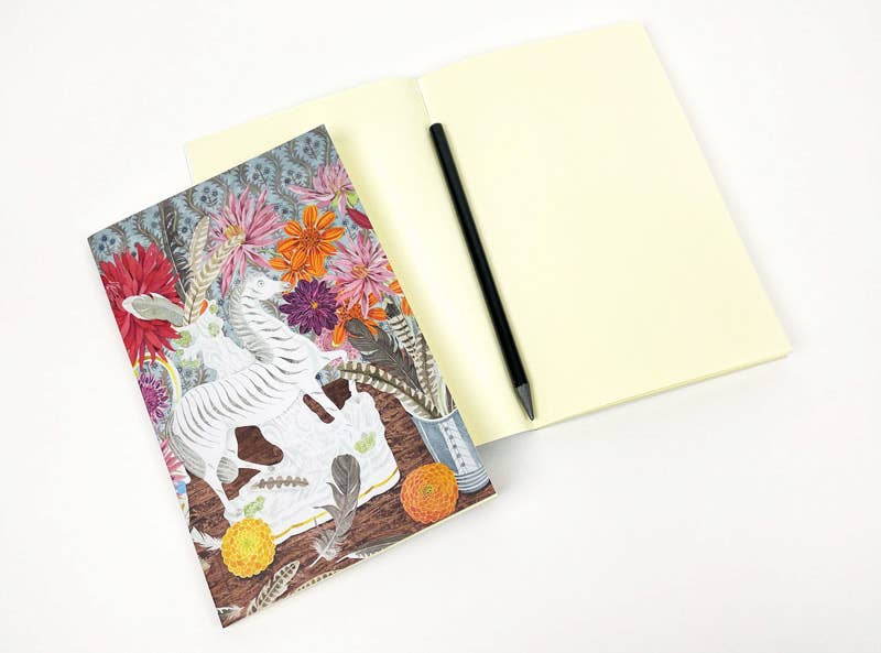 Ein offenes leeres Notizbuch mit einem schwarzen Stift liegt neben dem geschlossenen Art Angels Angie Lewin Notizbuch 'Zebra, Dahlien und Federn', beide auf weißem Hintergrund.