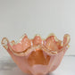 Die Murano Dream Dekoschale „Fazzoletto“ aus Murano-Glas in Rosa (H 20, Ø 22 cm) besticht durch gewellte, durchscheinende Ränder und präsentiert feinste italienische Glaskunst auf einer weiß-grau marmorierten Oberfläche vor hellem Hintergrund.