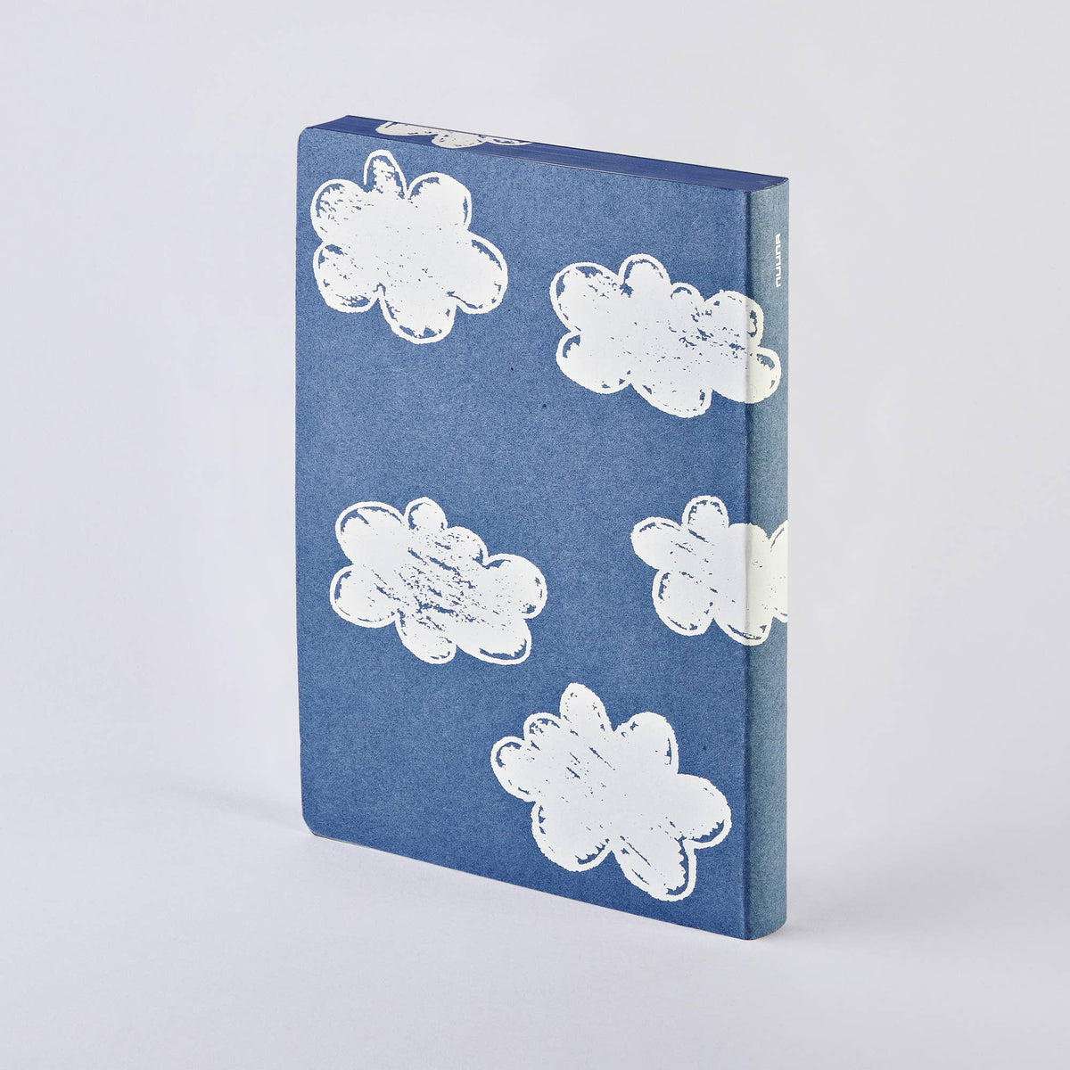 Das nuuna „Head In The Clouds“ Notizbuch Graphic L A5+ von nuuna steht aufrecht in einem blauen Hardcover-Einband und ist mit verspielten weißen Comic-Wolken verziert, die auf der Vorderseite und dem Buchrücken vor einem schlichten, hellen Hintergrund verteilt sind. Dieses Notizbuch aus recyceltem Denim und hochwertigem Papier verbindet umweltbewusste Materialien mit einem verspielten Design.