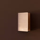 Eine rechteckige, perforierte burgunderrote Wandhalterung - die an ein Tinne Mia Bullet Journal A6 'Grid Burgunderrot' erinnert - ist an einer schlichten braunen Wand angebracht und wirft einen weichen Schatten nach rechts.