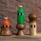 Drei leuchtende Flaschen mit verspielten Augen - orange, grün und beige - ruhen auf kupfernen Gefäßen vor einer braunen Wand und präsentieren das Natives Olivenöl extra mit Basilikum 200 ml von yiayia and friends auf einer rustikalen Holzoberfläche.