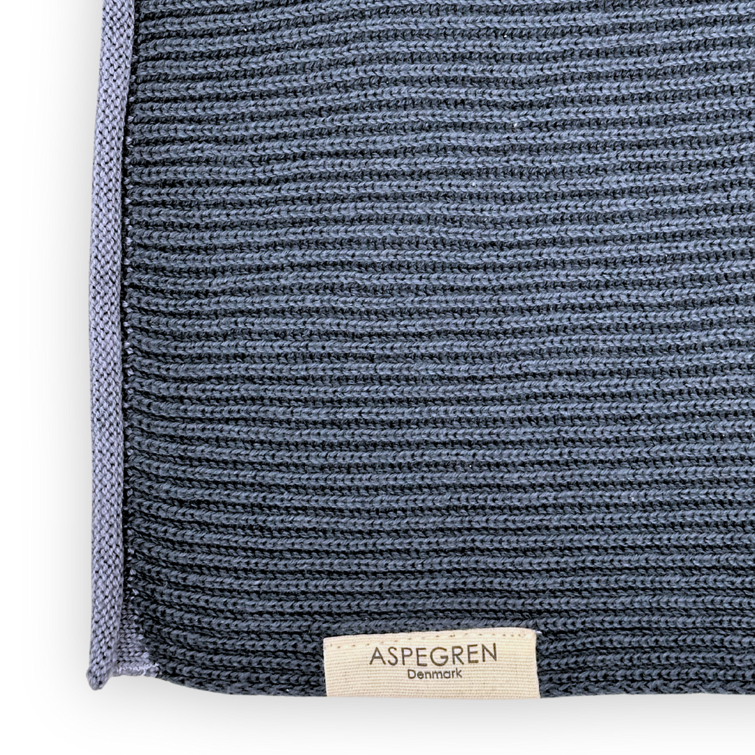 Eine Nahaufnahme eines strukturierten, tiefblauen Strickstoffs in nordischem Blau aus Bio-Baumwolle, mit einem hellgrauen Rand und einem kleinen beigen Etikett mit der Aufschrift „ASPEGREN Denmark“ am unteren Rand – ein elegantes Beispiel für Küchentextilien aus dem „Aspegren Denmark Premium 3er Küchentuchset“.